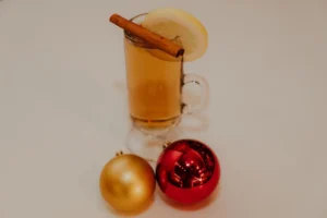 Cocktail with a cinnamon stick and lemon garnish surrounded by holiday ornaments