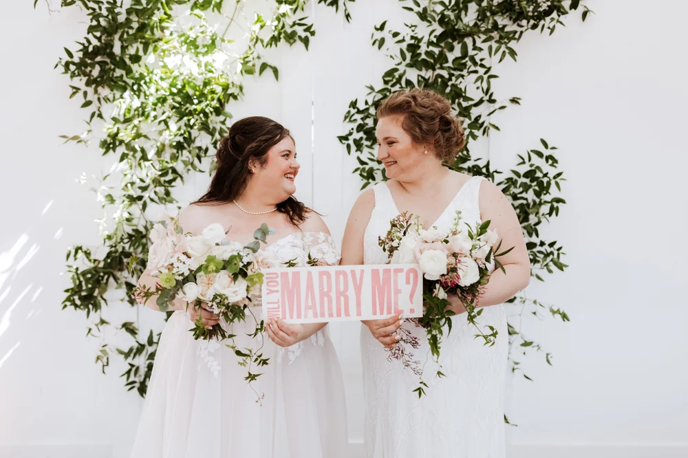 LGBTQ+ brides holding a marry me sign at 14TENN wedding venue in Nashville TN